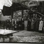 23 people gather around a cornerstone, A.D. 1943. They are wearing long coats and hats. Some of the men on the left have removed their hats for the picture.