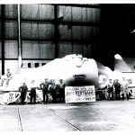 9 men stand infront of a hot metal car, they manufactured at the factory for Algoma Steel.