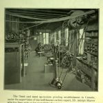 Two men operating equipment in a grinding shop. There are many pulleys and ropes, with work stations on either side.