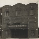 Brick building with scalloped edges at the roof. Three windows face the street above the entrance to the theatre. There is one window on either side of the entrance.