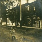 A child stands on a dirt road in front of the Doctors office.