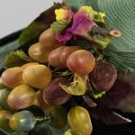 green straw hat with faux grapes affixed to top.