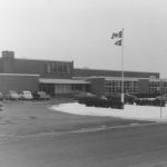 Dundana School exterior. Cars line the circular parking lot and a flagpole stands out front.