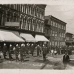 photographic postcard of soldiers and a band marching down the street in front of Laing's Grocery.