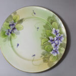 Plate. Light green background, violets, leaves, gold around leaves.