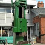 The steam hammer, painted green, sits in front of its new home at the Museum.