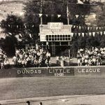 The little league scoreboard with a crowd of spectators watching the game